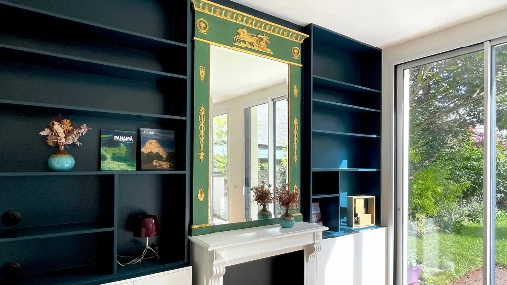 Bibliothèque sur-mesure en MDF peint bleu encadrant une cheminée rénovée et son miroir, chantier Bruyères à Asnières